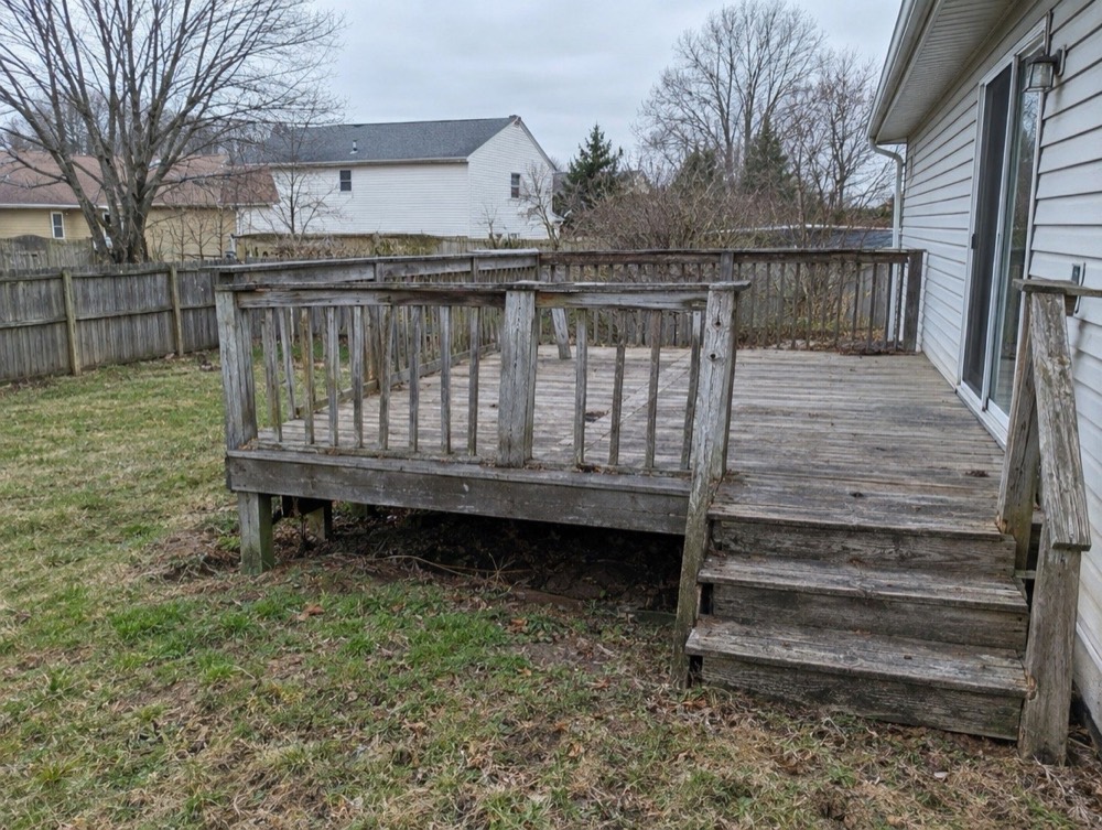 Weathered gray wood deck with worn boards and a loose wooden railing